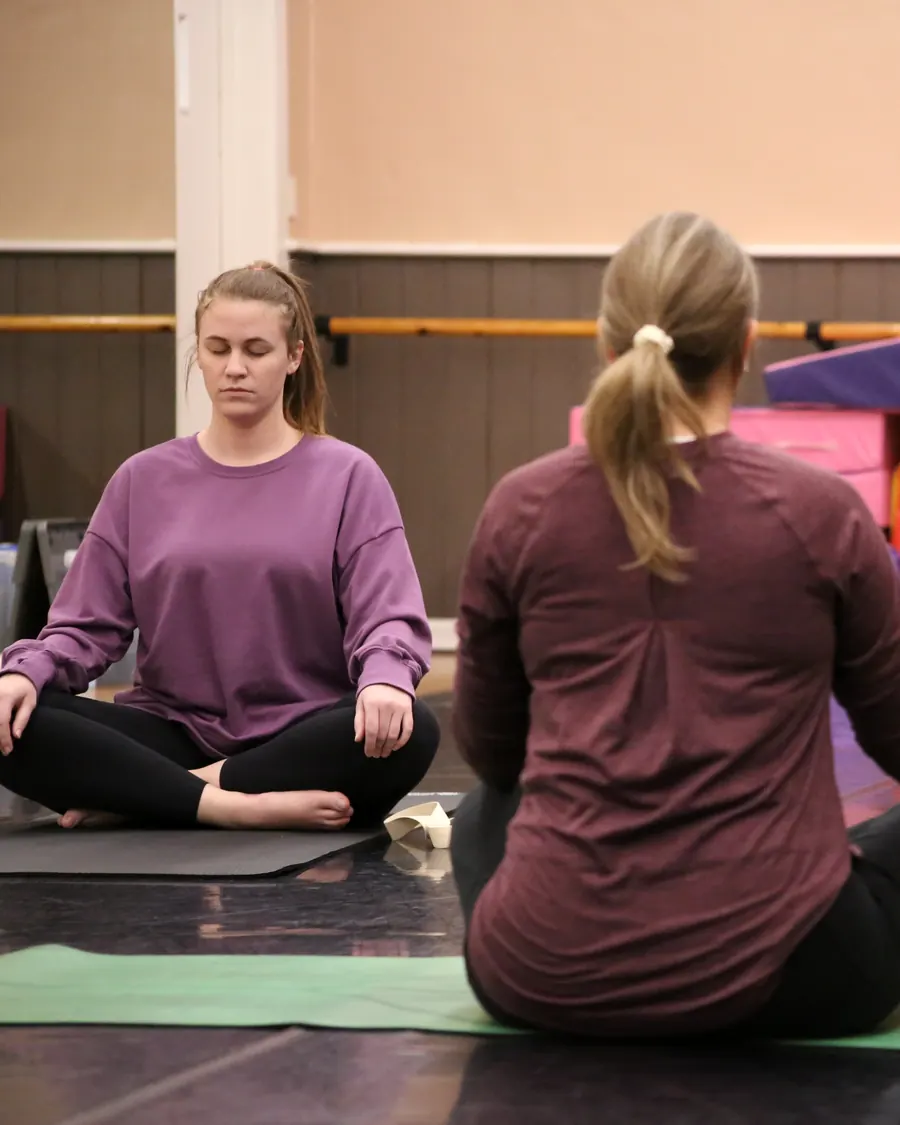 An adult yoga student seated cross-legged in meditation beside the instructor at the Elevate studio