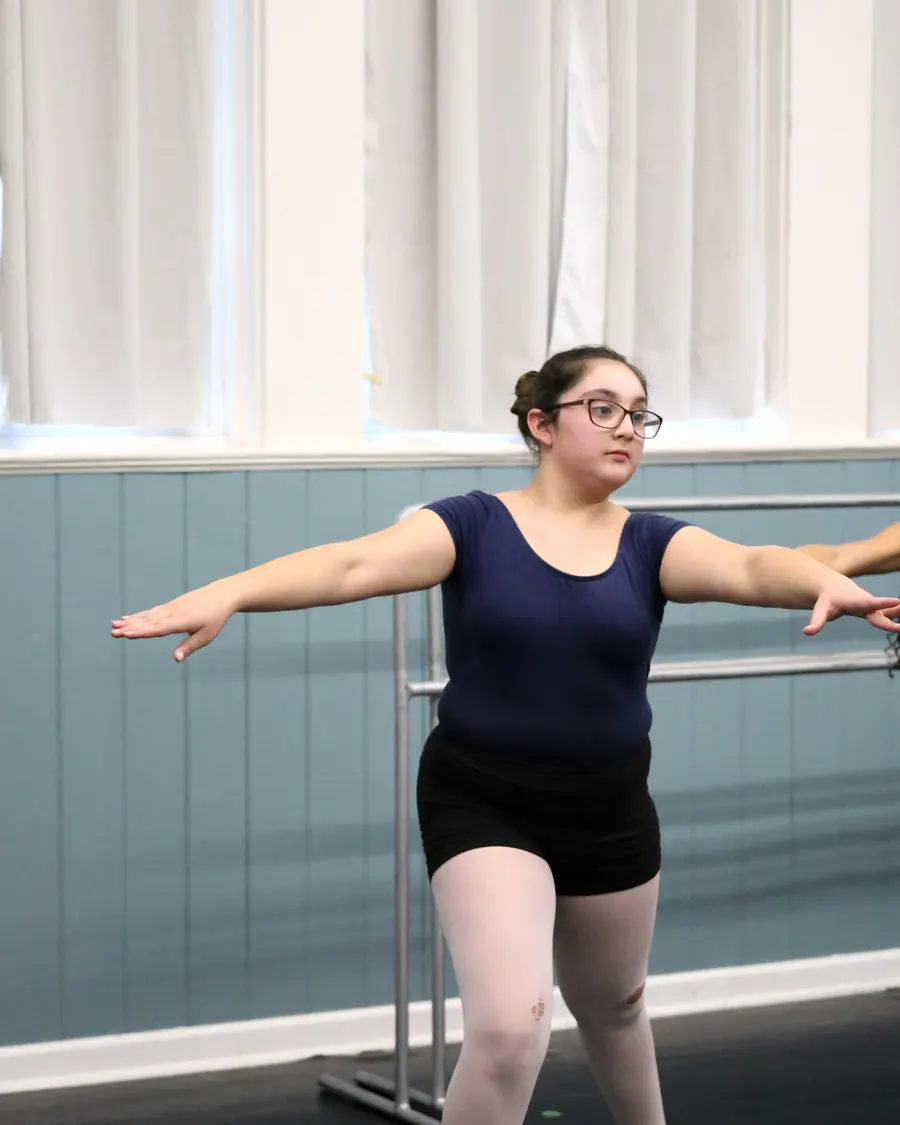 A Jazz 3-4 dancer mid-step with arms in second, a classmate echoing the move behind her