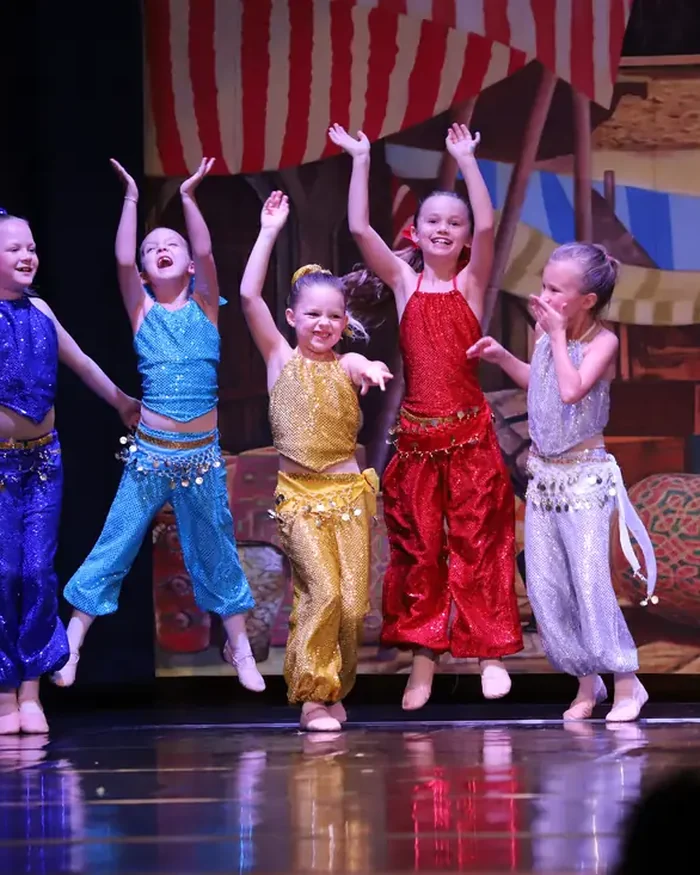 Young dancers in sequined harem costumes jumping with their arms raised