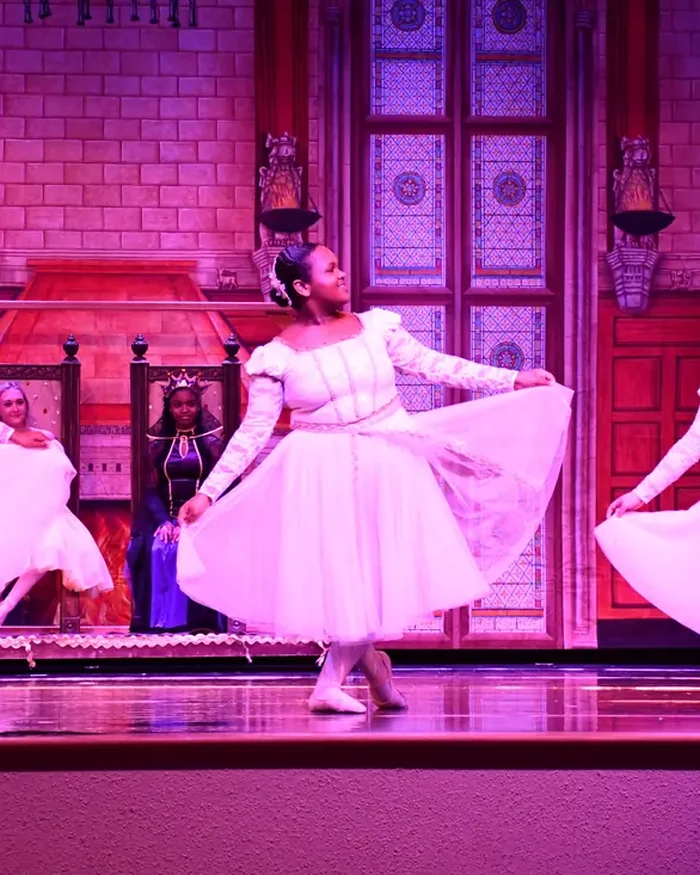 A dancer in a pale gown turning in front of a painted palace interior