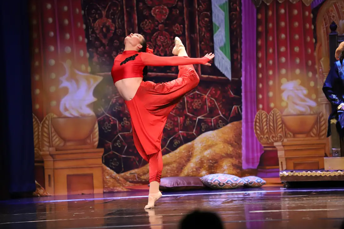 A dancer in red silk arching back toward her raised foot on a palace set