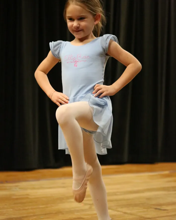 A young dancer with her hands on her hips lifting one knee high in a passe balance