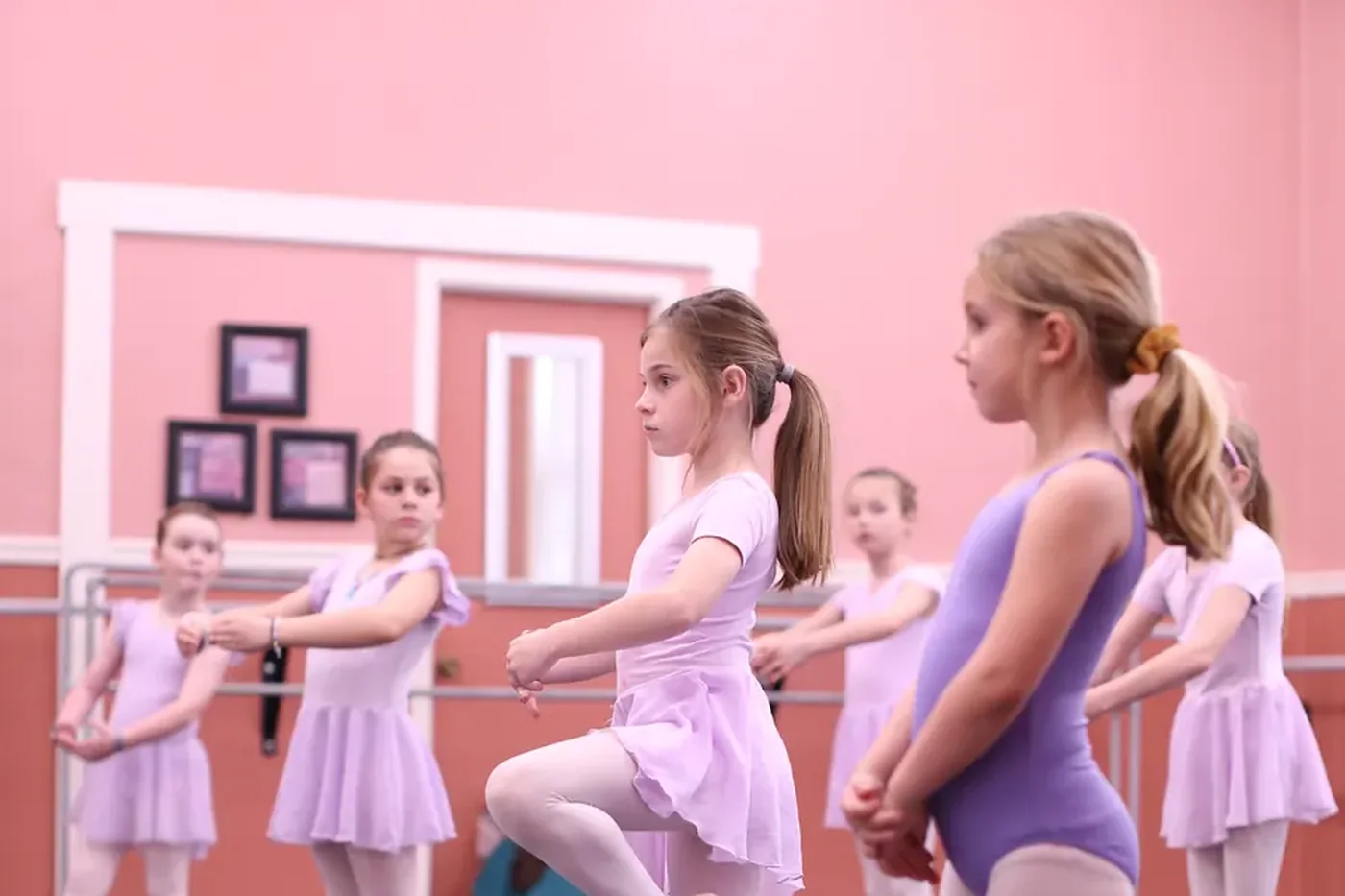 Young dancers in lilac leotards balancing on one leg together during a ballet class