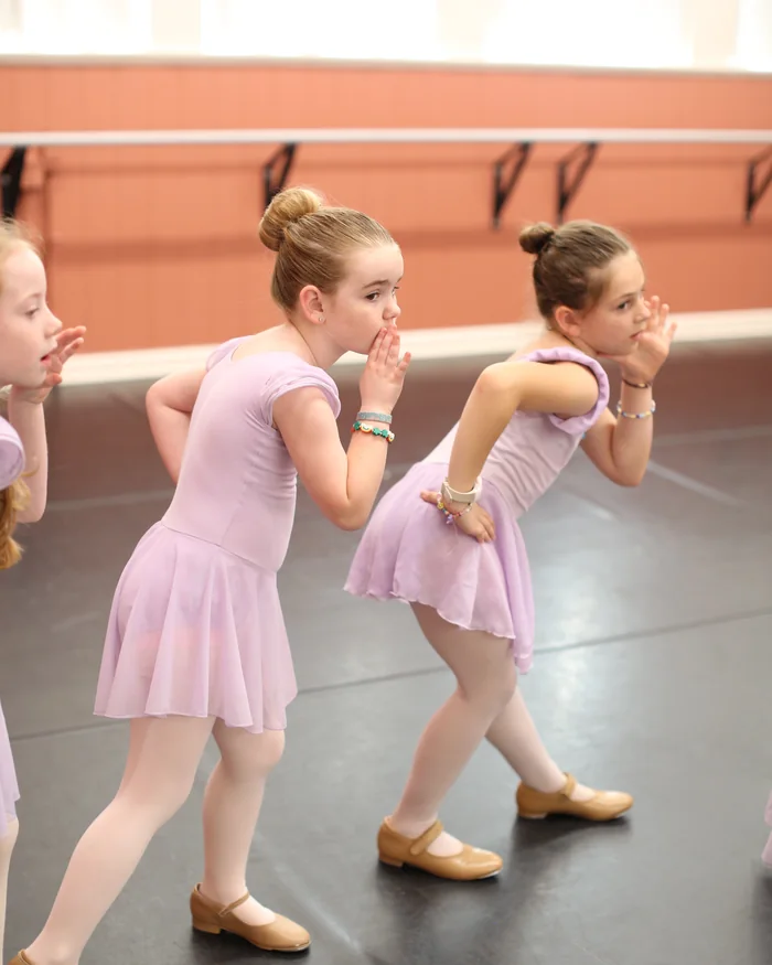 Two young dancers in pink leotards practising a step together on the studio floor