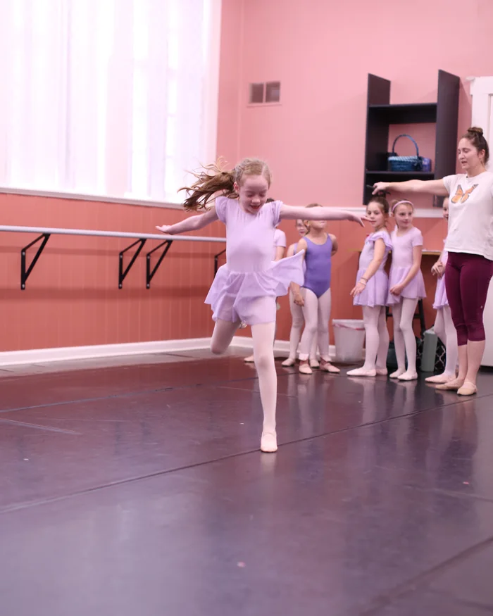 A young dancer in a lilac leotard travelling across the floor with her arms extended