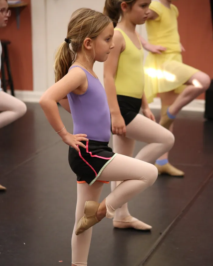 Dancers in a jazz class balancing on one leg with their hands on their hips