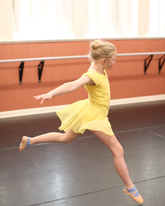 A dancer in a lemon leotard and skirt leaping across the studio floor