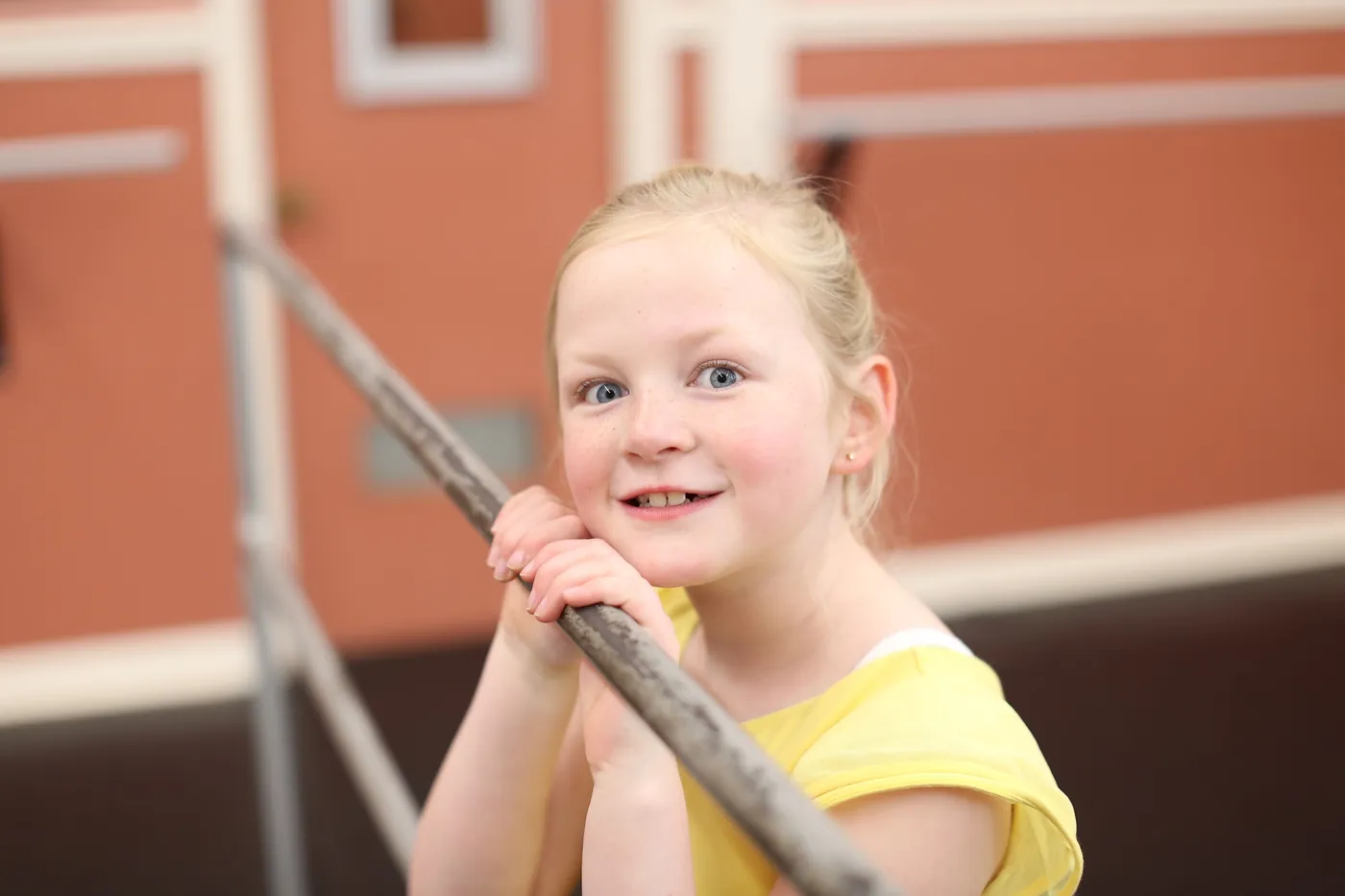 A smiling dancer in a lemon leotard resting her hands on the ballet barre