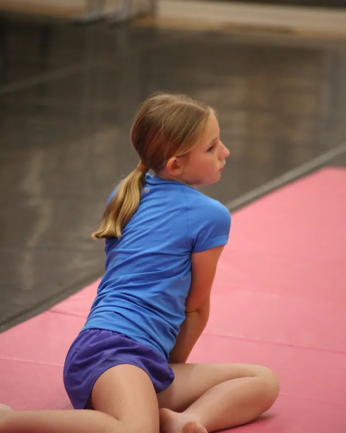 A dancer in a blue shirt sitting on the tumbling mat between turns