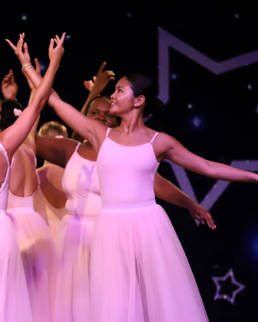 An Elevate dancer in a pale pink dress reaching one arm out on the showcase stage