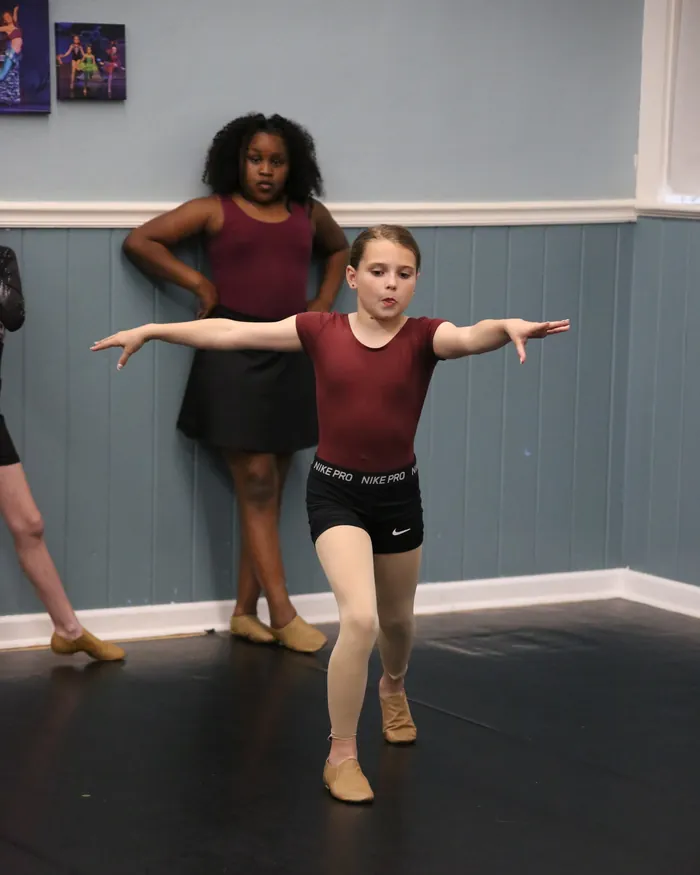 A jazz dancer in a maroon leotard balancing on one leg with her arms stretched out
