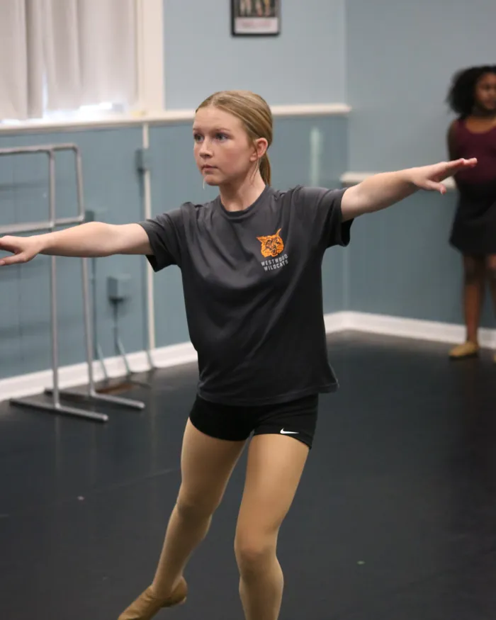 A jazz dancer in a gray t-shirt stepping into a lunge with both arms out