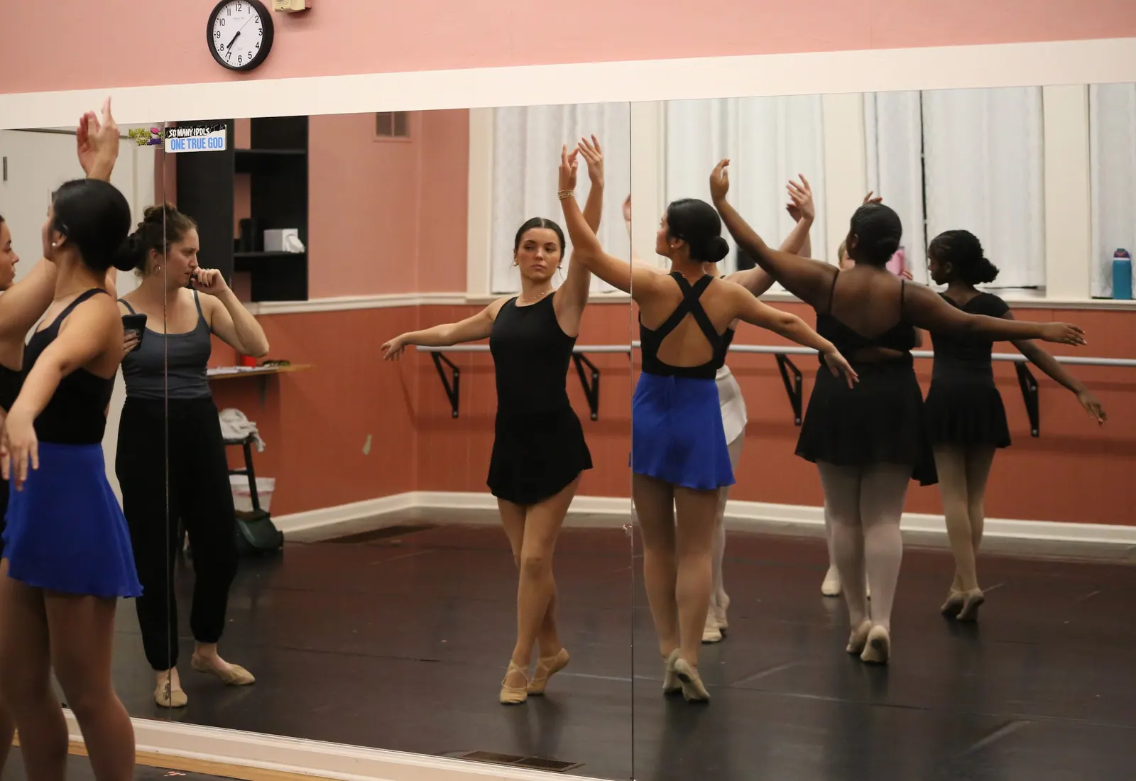 Ballet dancers in black leotards moving through a center combination with their arms raised