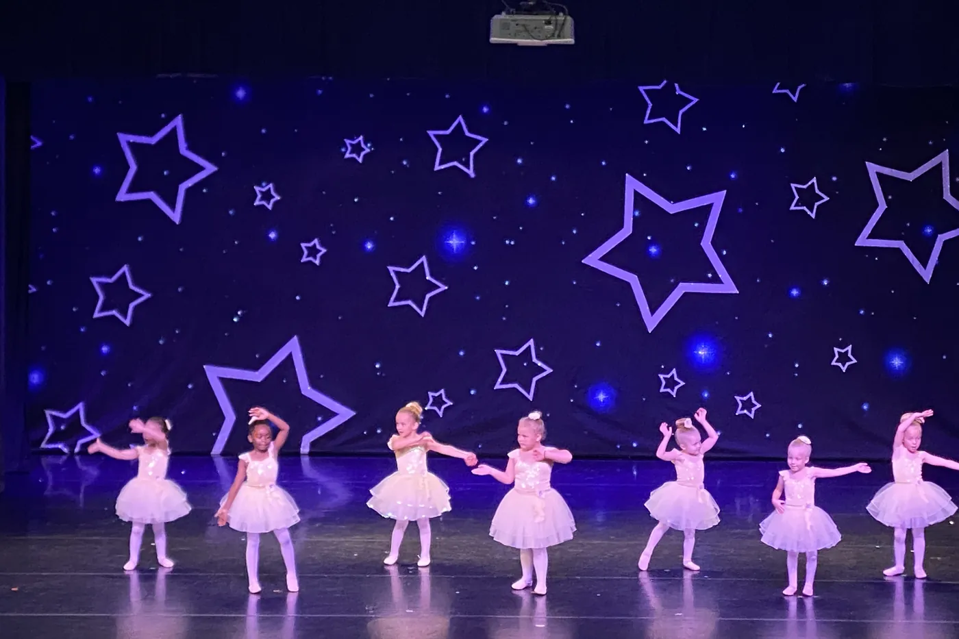 A full line of Elevate's youngest dancers in white tutus spread right across the Spring Showcase stage under the starry backdrop