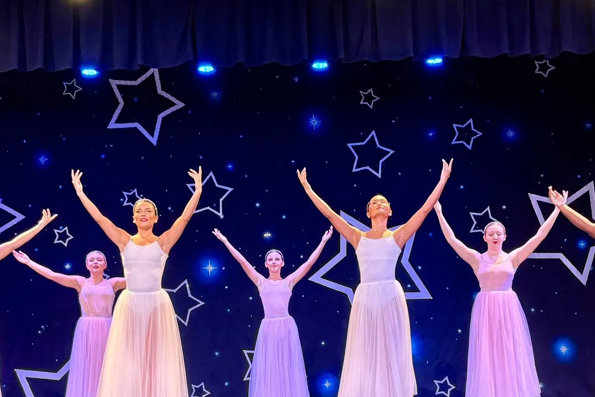 Elevate dancers in pastel floor-length tutus, both arms lifted, held on the last pose of their showcase number