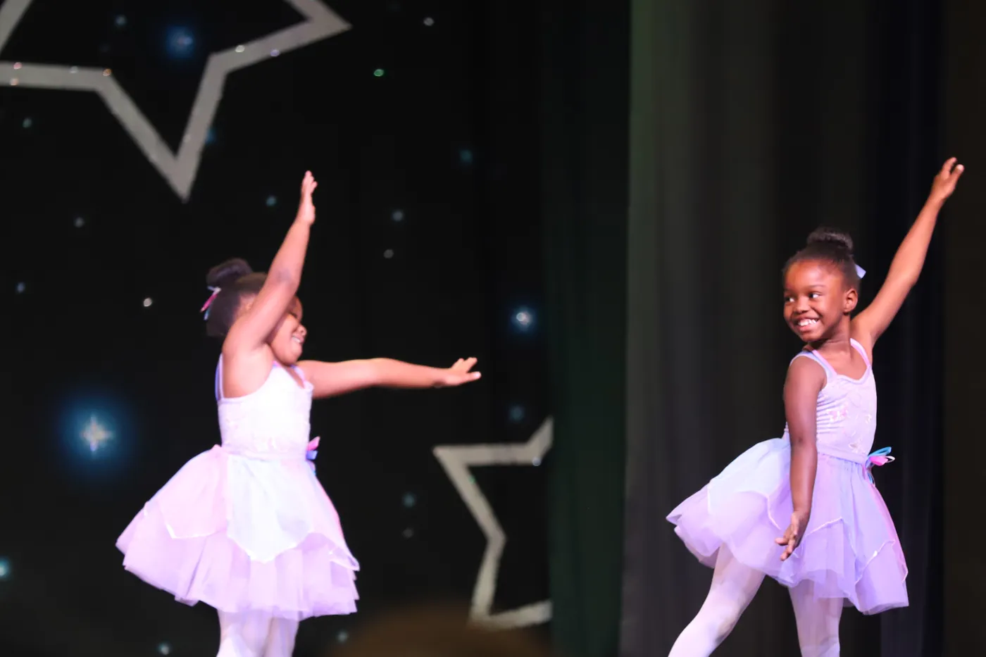 Two of Elevate's youngest dancers in white and lavender tutus, arms lifted, on the showcase stage