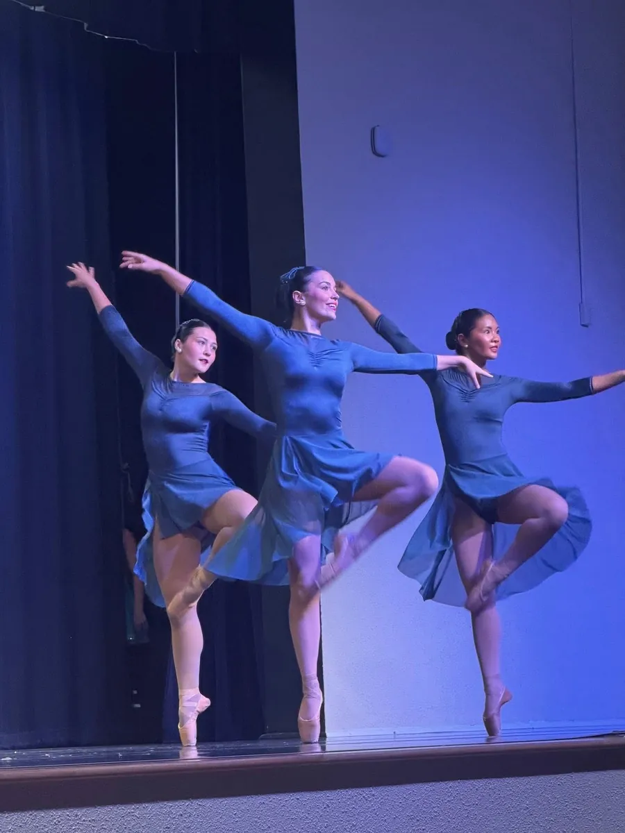 Three Elevate dancers in blue costumes holding a balance on pointe in a blue stage wash