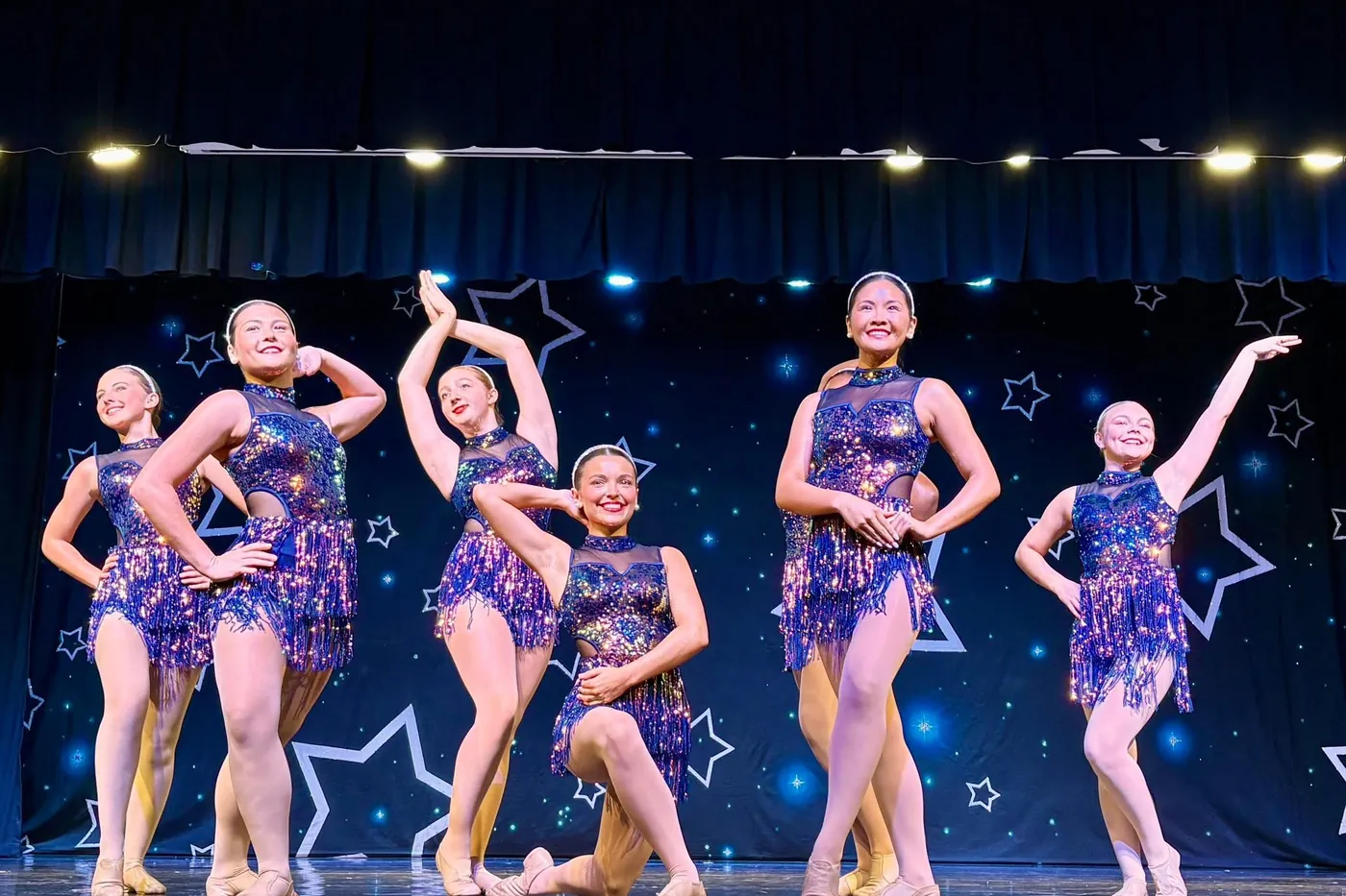 A line of Elevate teen dancers in blue and purple sequined costumes posing together at the end of a jazz number