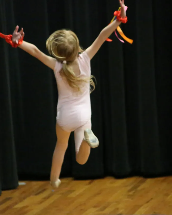 A young dancer jumping on the studio floor with colorful ribbons streaming from both hands